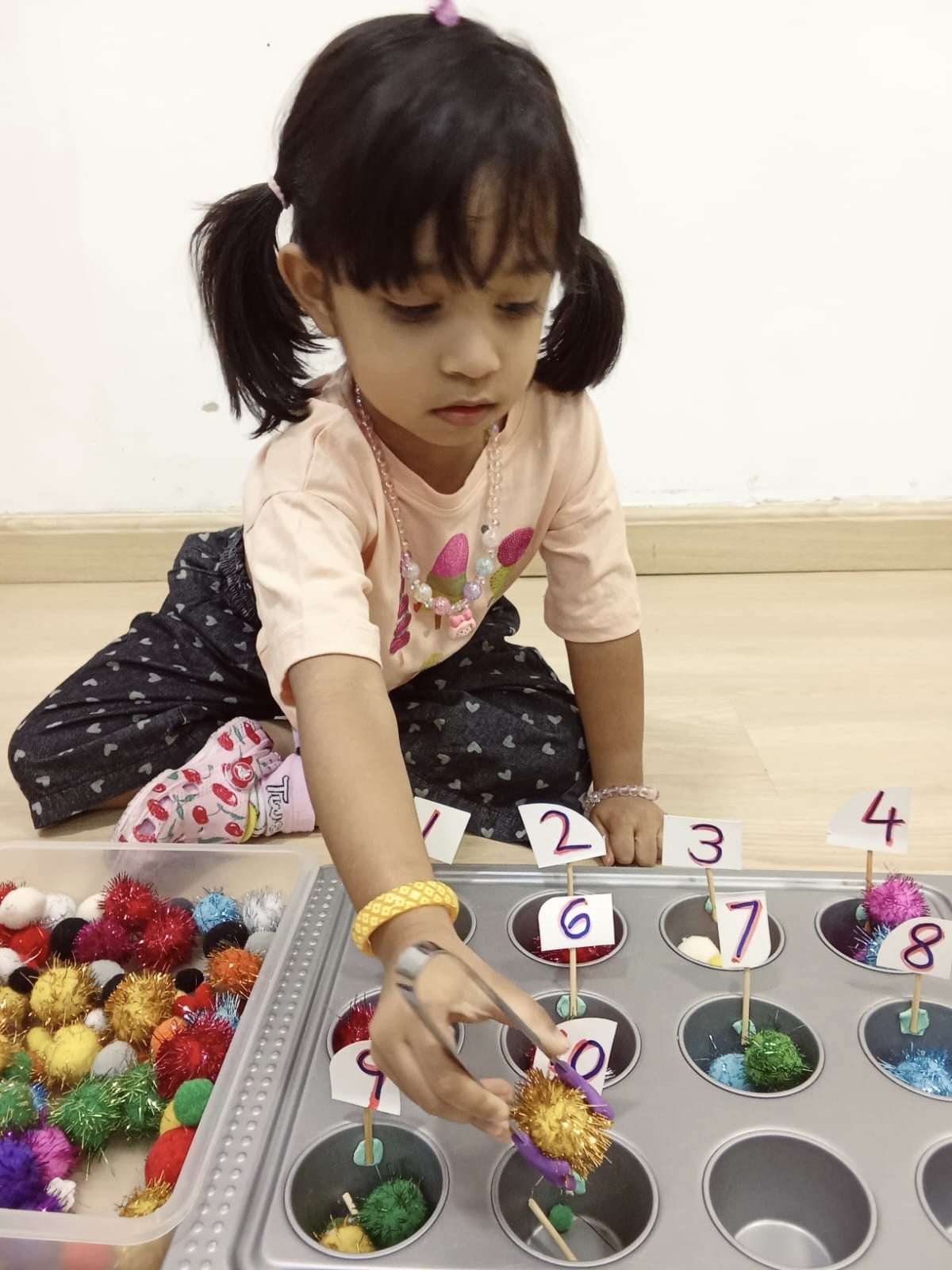 A child counting coloured pom-poms into numbered cups